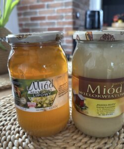 Kolorowe zdjęcie przedstawiające dwa Słoiki z miodem z etykietą oraz pieczątką lokalnego wytwórcy – pszczelarza.