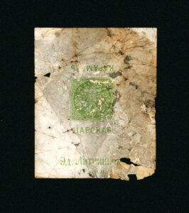 Zniszczony fragment papierowej banderoli z butelki alkoholu z czasów carskiej Rosji, zachowany w postaci małego, nieregularnego skrawka. Na pożółkłym i popękanym papierze widoczny jest zielony nadruk z dwugłowym orłem oraz cyrylicą. Można odczytać m.in. napis „ЦАРСКАЯ” oraz fragment „Эд. Литринг”, prawdopodobnie oznaczenie producenta lub miejsca rozlewu. Papier jest silnie zabrudzony, z licznymi plamami, pęknięciami i ubytkami. Na środku widoczny znak wodny „CZAS A.R.T.”.