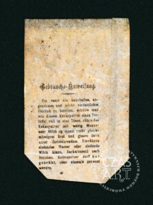 Odwrotna strona zniszczonej etykiety kakao z przełomu XIX i XX wieku z widoczną instrukcją użycia w języku niemieckim. Na pożółkłym, zabrudzonym i popękanym papierze widnieje nagłówek „Gebrauchs-Anweisung”, a poniżej drukowany tekst opisujący sposób przygotowania napoju kakaowego poprzez zalanie proszku wrzącą wodą lub mlekiem. Papier nosi liczne ślady starzenia, przebarwienia i ubytki w dolnej części. W prawym dolnym rogu widoczny jest znak wodny „CZAS A.R.T.”
