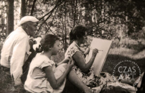 Czarno-biała archiwalna fotografia wykonana podczas pleneru malarskiego w okolicach Wschowy pod koniec lat 50. XX wieku. Na pierwszym planie siedzi Matylda Szymczakowska, rysująca na kartce umieszczonej na sztaludze. Obok niej stoi młoda Elżbieta Lewandowska, uważnie obserwująca pracę matki. Za nimi widoczny jest Onufry Kubicki, pochylony i przyglądający się rysunkowi. W tle drzewa i naturalny krajobraz, w którym odbywały się zajęcia plenerowe Klubu Twórców Amatorów działającego przy Domu Kultury we Wschowie.