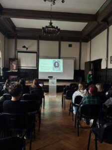 Slajd przedstawiający scenę palenia na stosie podczas procesu o czary, oglądany przez uczestników wykładu.