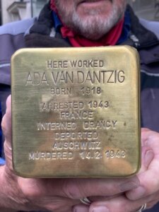 Zbliżenie na mosiężny kamień pamięci (Stolperstein) trzymany w dłoniach. Na powierzchni widoczna jest wygrawerowana inskrypcja upamiętniająca Adę Van Dantzig, zawierająca informacje o jej losie – od urodzenia, przez aresztowanie i deportację, po śmierć w Auschwitz w 1943 roku.