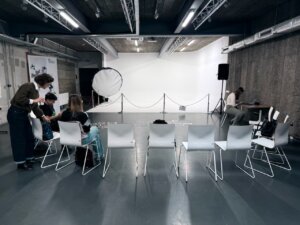 Zdjęcie czarno białe przedstawiające salę Wykładowa, W tle projektor oraz kilku uczestników którzy stoją przy krzesłach.