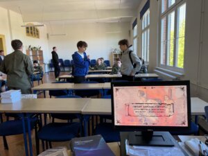 Wnętrza sali lekcyjnej na przodzie fotografii ekran monitora z pierwszą stroną prezentacji.