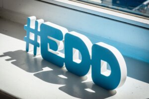 Trójwymiarowy napis „#EDD” w kolorze biało-niebieskim ustawiony na parapecie przy oknie, oświetlony światłem dziennym, rzucający wyraźny cień na powierzchnię