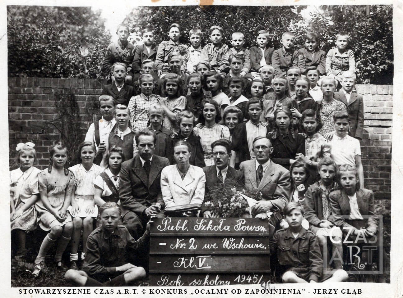 Czarno-biała fotografia grupowa przedstawiająca uczniów i nauczycieli Publicznej Szkoły Powszechnej nr 2 we Wschowie. Zdjęcie wykonano w roku szkolnym 1945/1946, tuż po zakończeniu II wojny światowej. Kilkudziesięcioro dzieci oraz czworo nauczycieli pozuje przed ceglanym murem i drzewami. Na tablicy umieszczonej na pierwszym planie widnieje napis: „Publ. Szkoła Powsz. Nr 2 we Wschowie, Kl. V, Rok szkolny 1945/46”. Fotografia została przekazana do konkursu „Ocalmy od zapomnienia” przez Jerzego Głąba i stanowi cenne świadectwo odbudowy życia szkolnego oraz społecznego we Wschowie po wojnie.